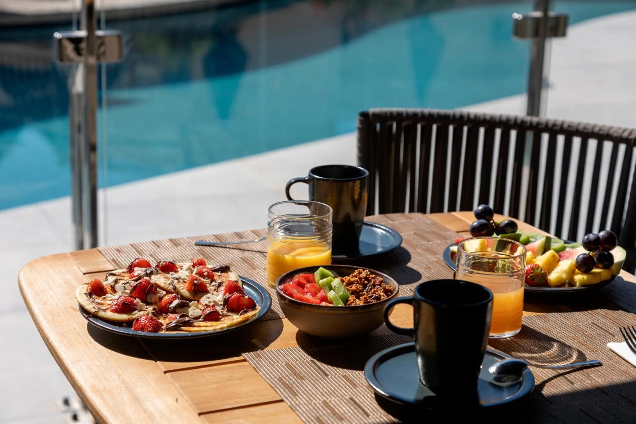 Une table en bois présente un petit-déjeuner avec des crêpes, des fruits et des boissons.