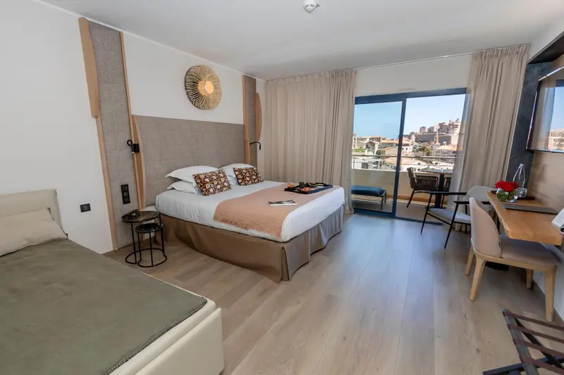 Une chambre lumineuse avec un lit double et un bureau près d'une baie vitrée.