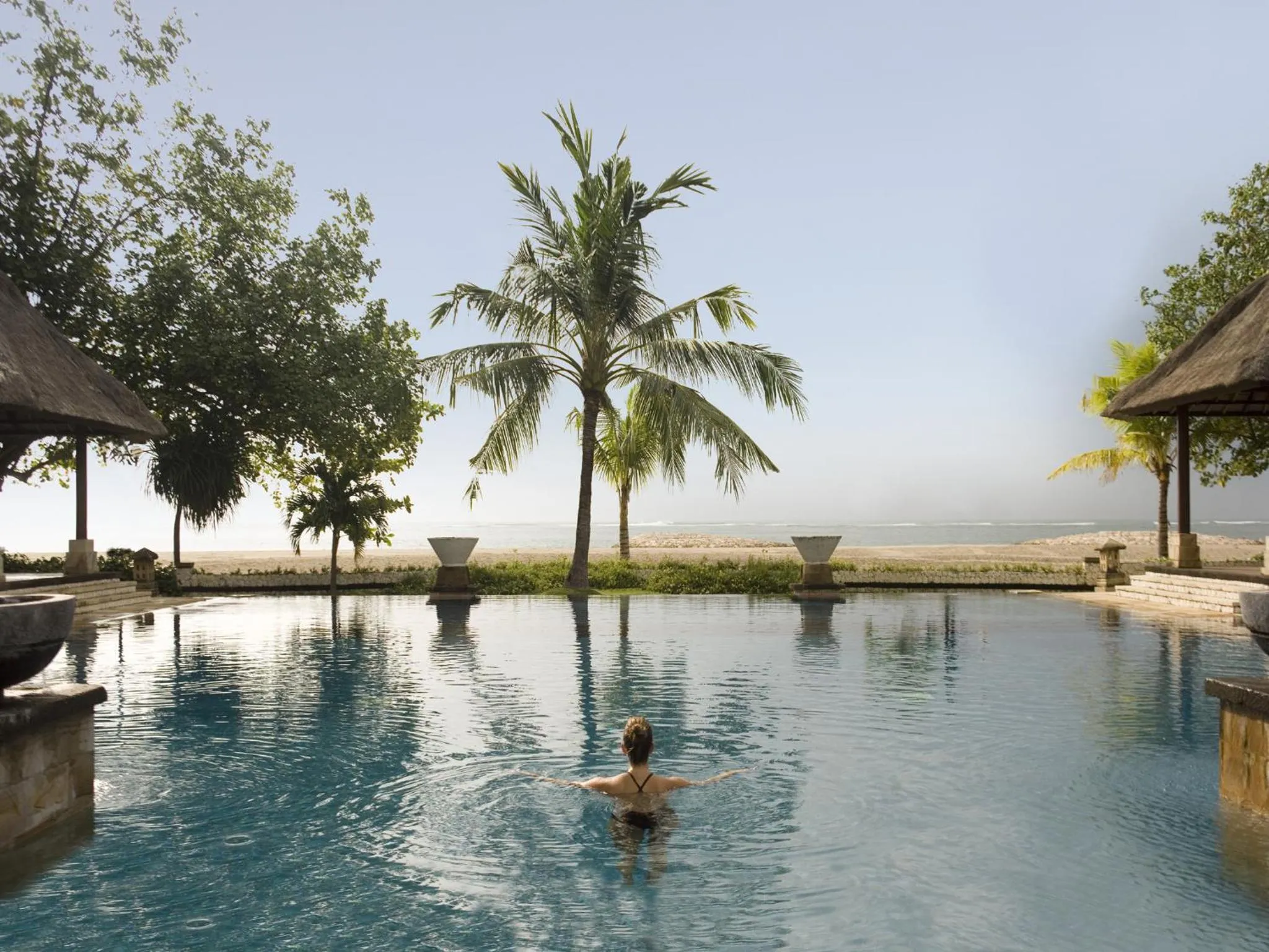 Une personne nage dans une piscine rectangulaire bordée de verdure et donnant sur la mer.