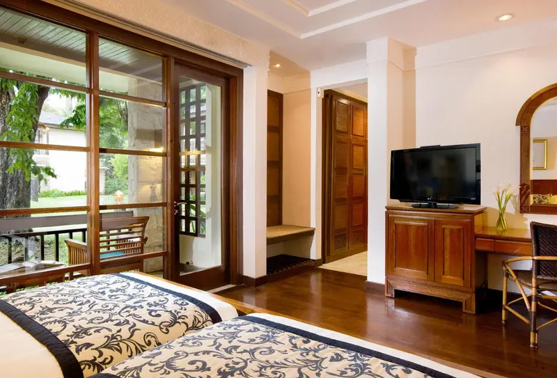 Une chambre avec un lit recouvert d'une courtepointe bleue et blanche, un bureau en bois et un accès à une terrasse.