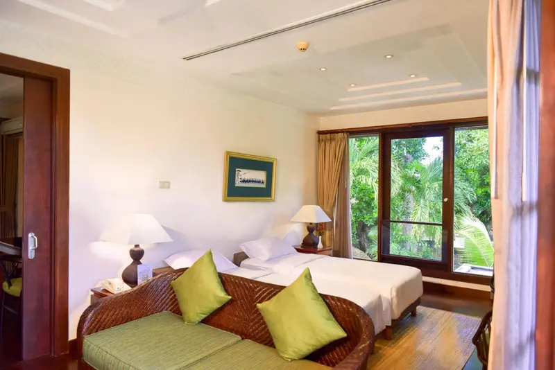Une chambre lumineuse avec un canapé et un lit donnant sur une végétation luxuriante.