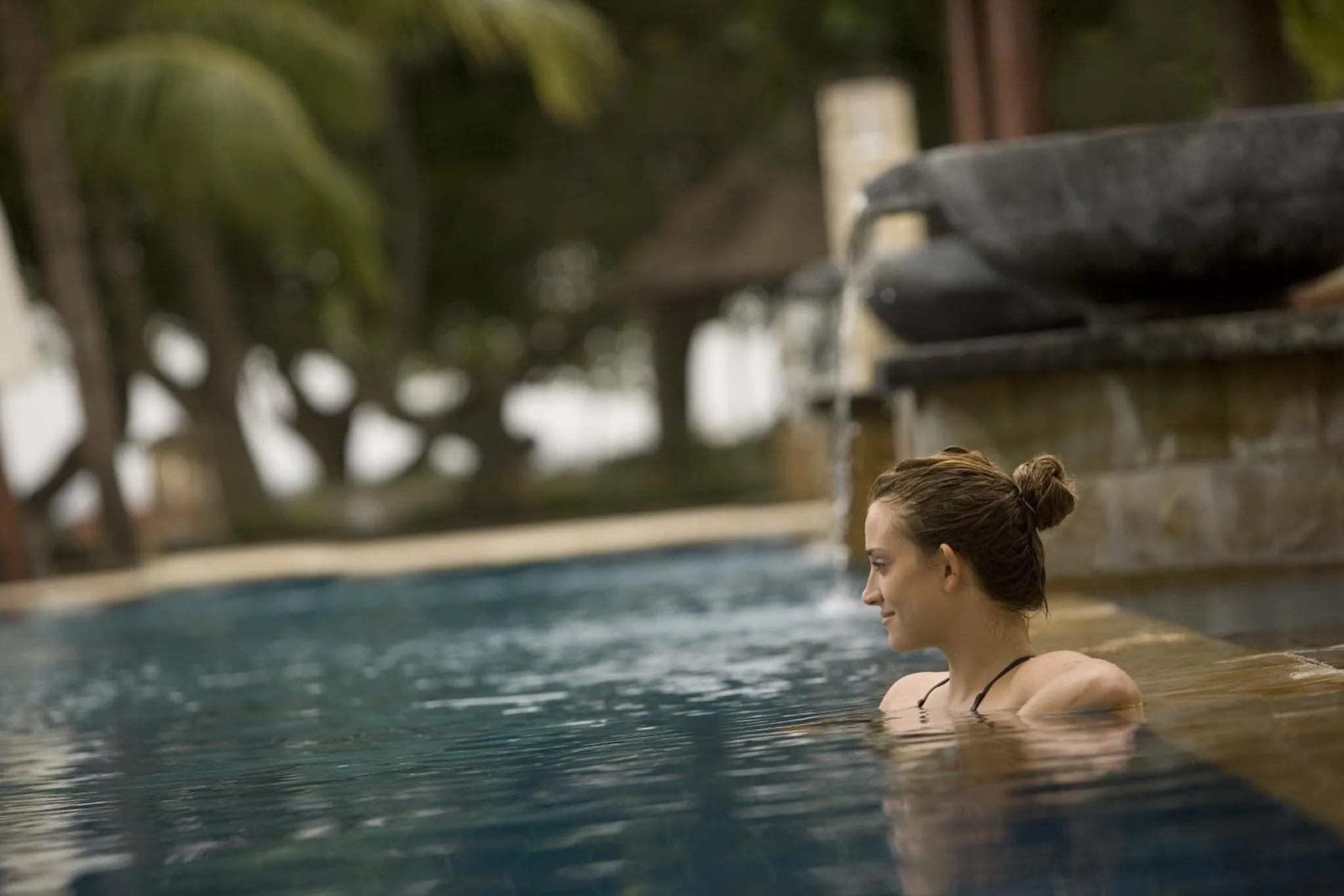 Une femme se détend au bord d'une piscine en regardant vers l'extérieur.
