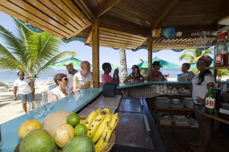 Un comptoir de bar en plein air avec des clients et un barman sur une plage ensoleillée.