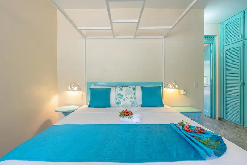 Une chambre lumineuse avec un grand lit recouvert d'une courtepointe turquoise et de fleurs.