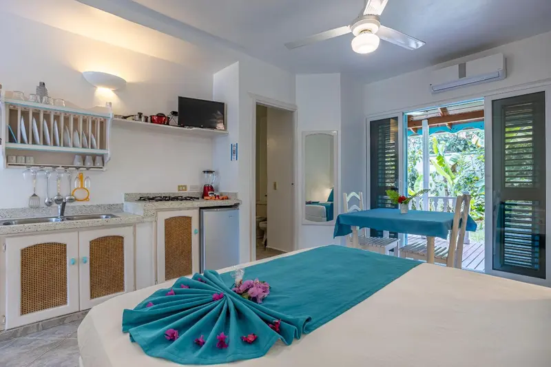 Une chambre lumineuse avec un lit recouvert d'un tissu bleu turquoise et une kitchenette équipée.