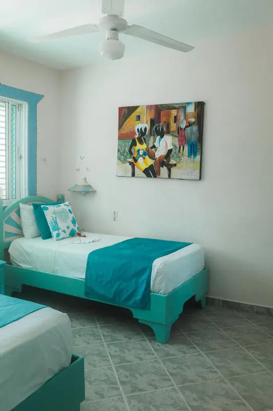 Une chambre lumineuse avec un lit turquoise et une décoration murale colorée.