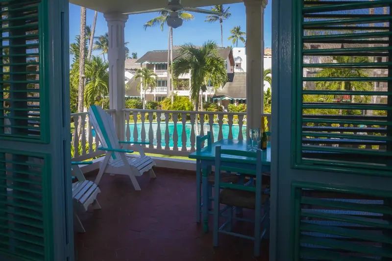 Une terrasse ombragée donne sur une piscine et une végétation luxuriante.