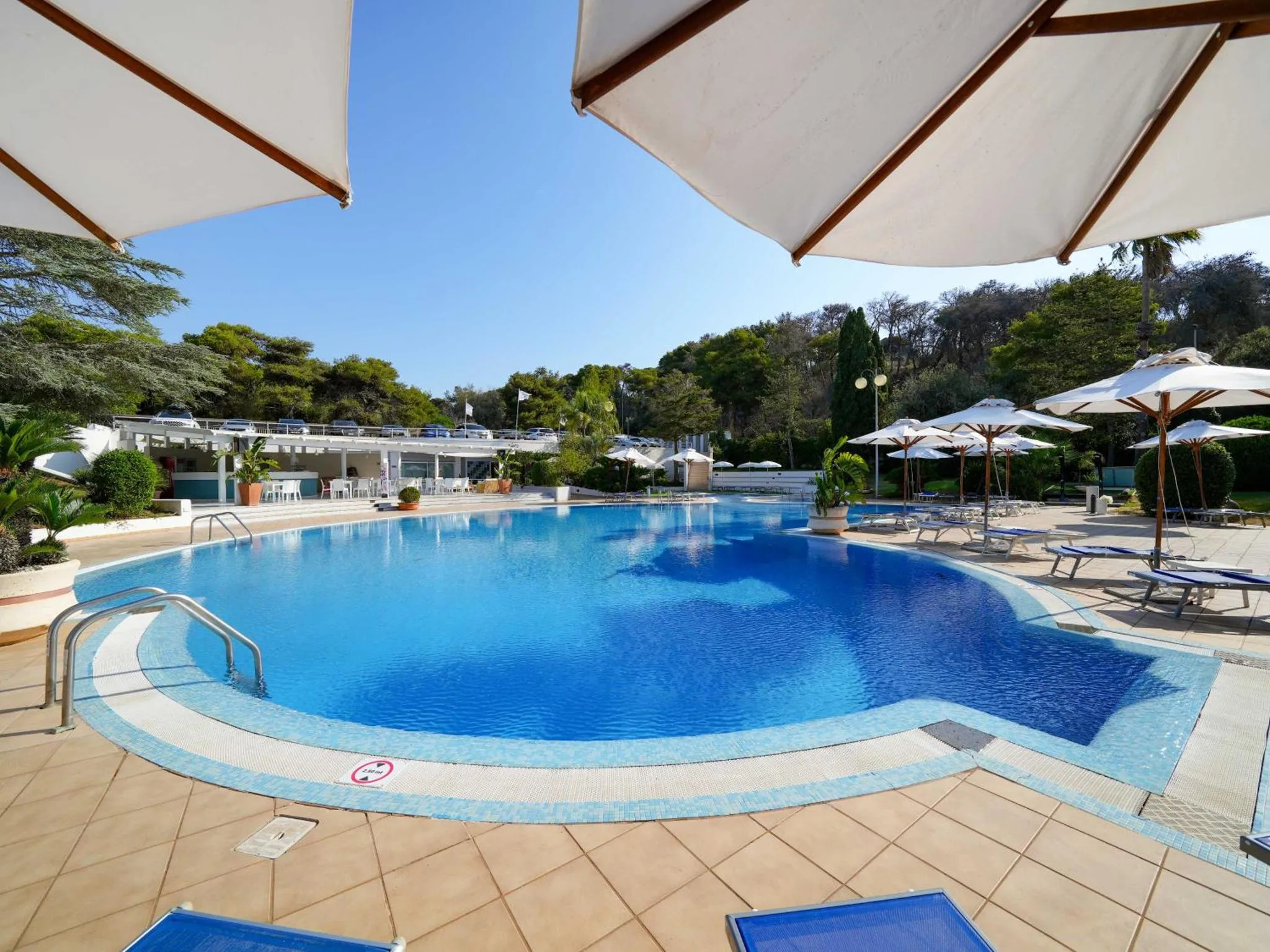 Une piscine bleue bordée d'une terrasse avec des transats et des parasols.
