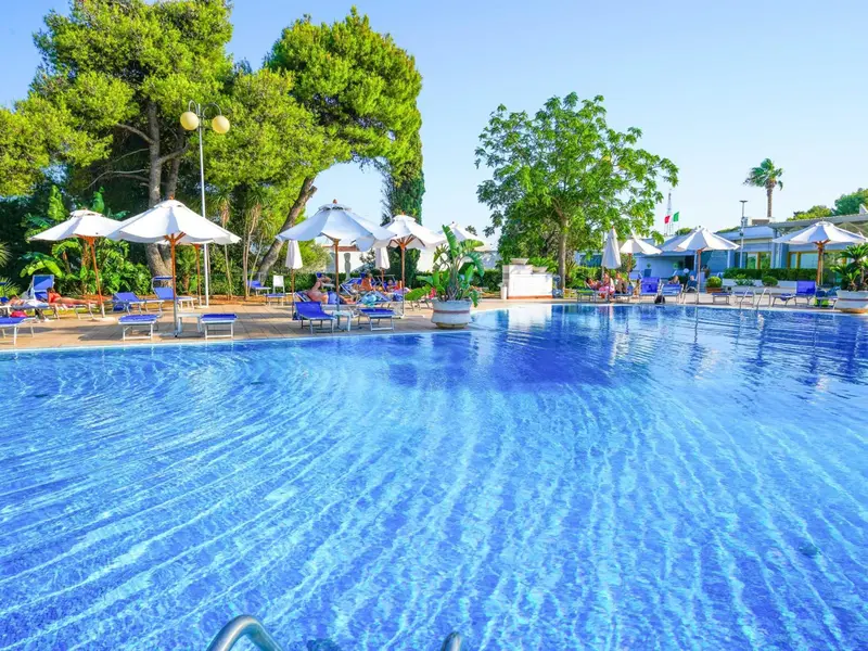 Une piscine turquoise bordée de transats blancs sous des parasols.