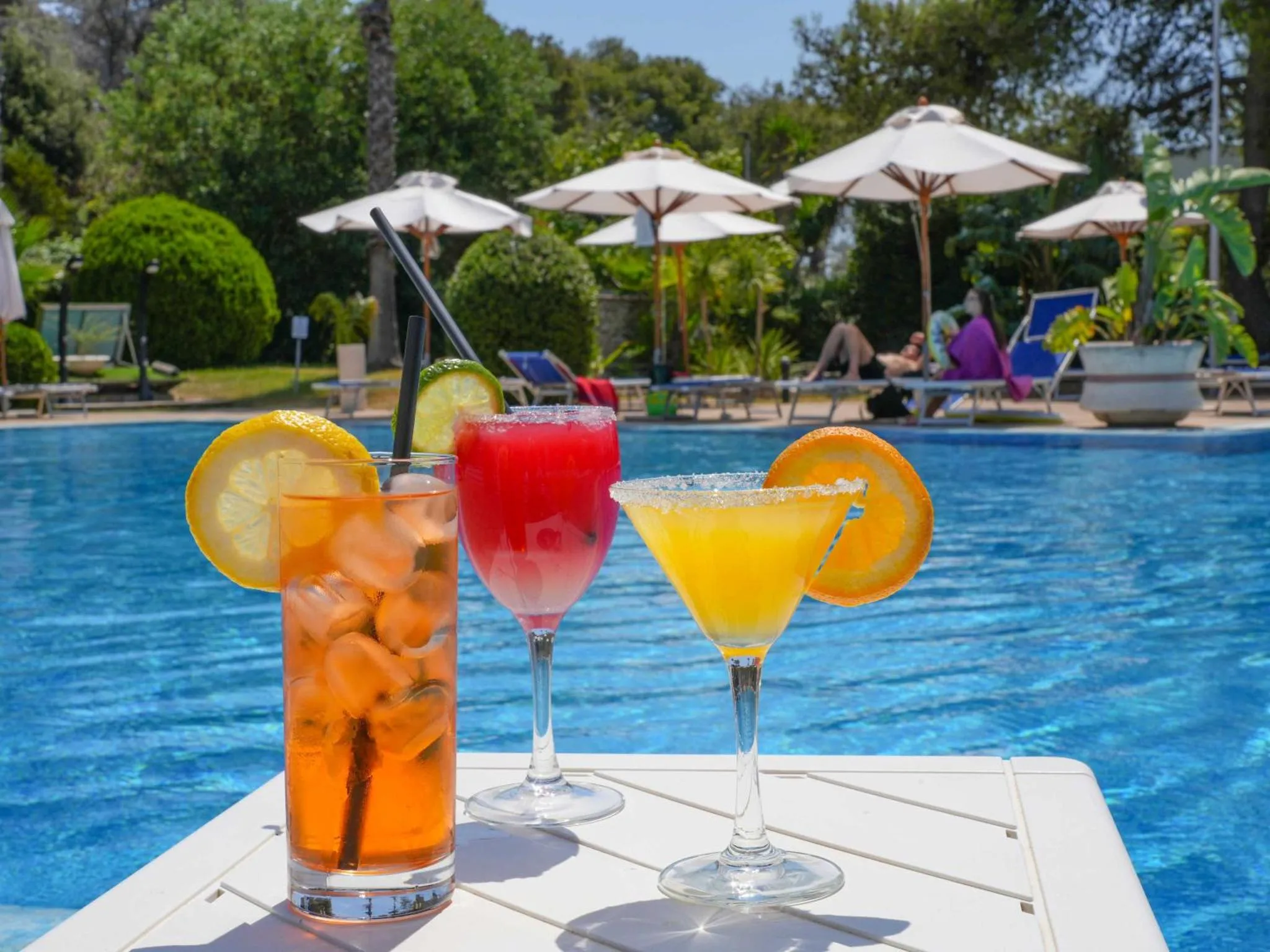 Des cocktails colorés sont présentés au bord d'une piscine ensoleillée.