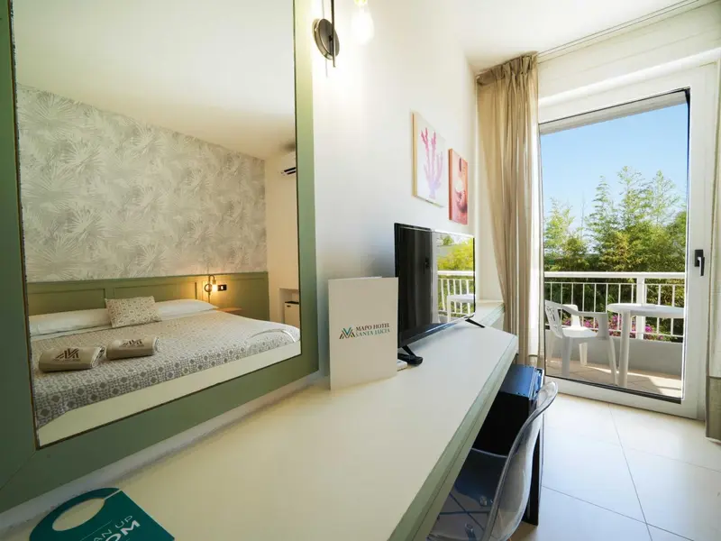 Chambre lumineuse avec un lit double et un balcon donnant sur la végétation.