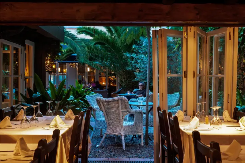 Une salle à manger lumineuse s'ouvre sur une cour verdoyante avec des tables.