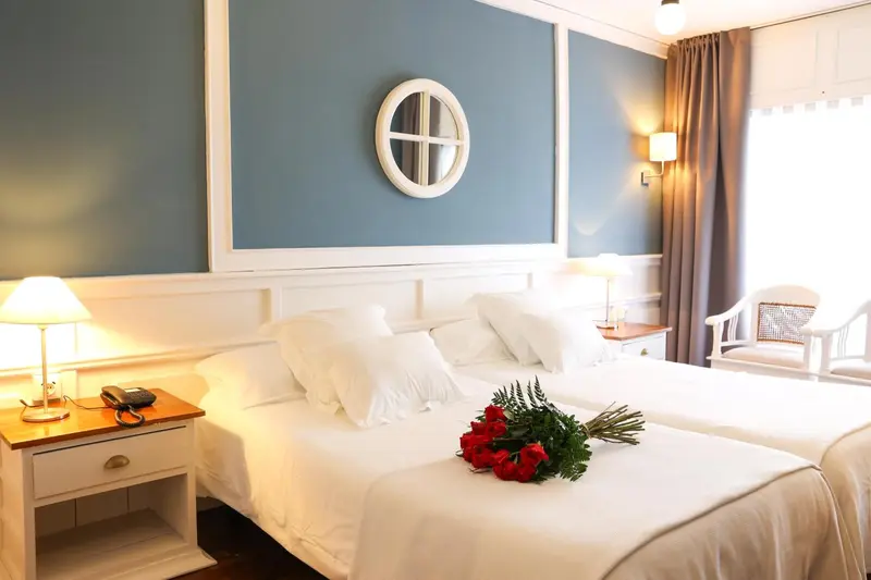 Une chambre lumineuse avec un grand lit recouvert de draps blancs et de fleurs rouges.