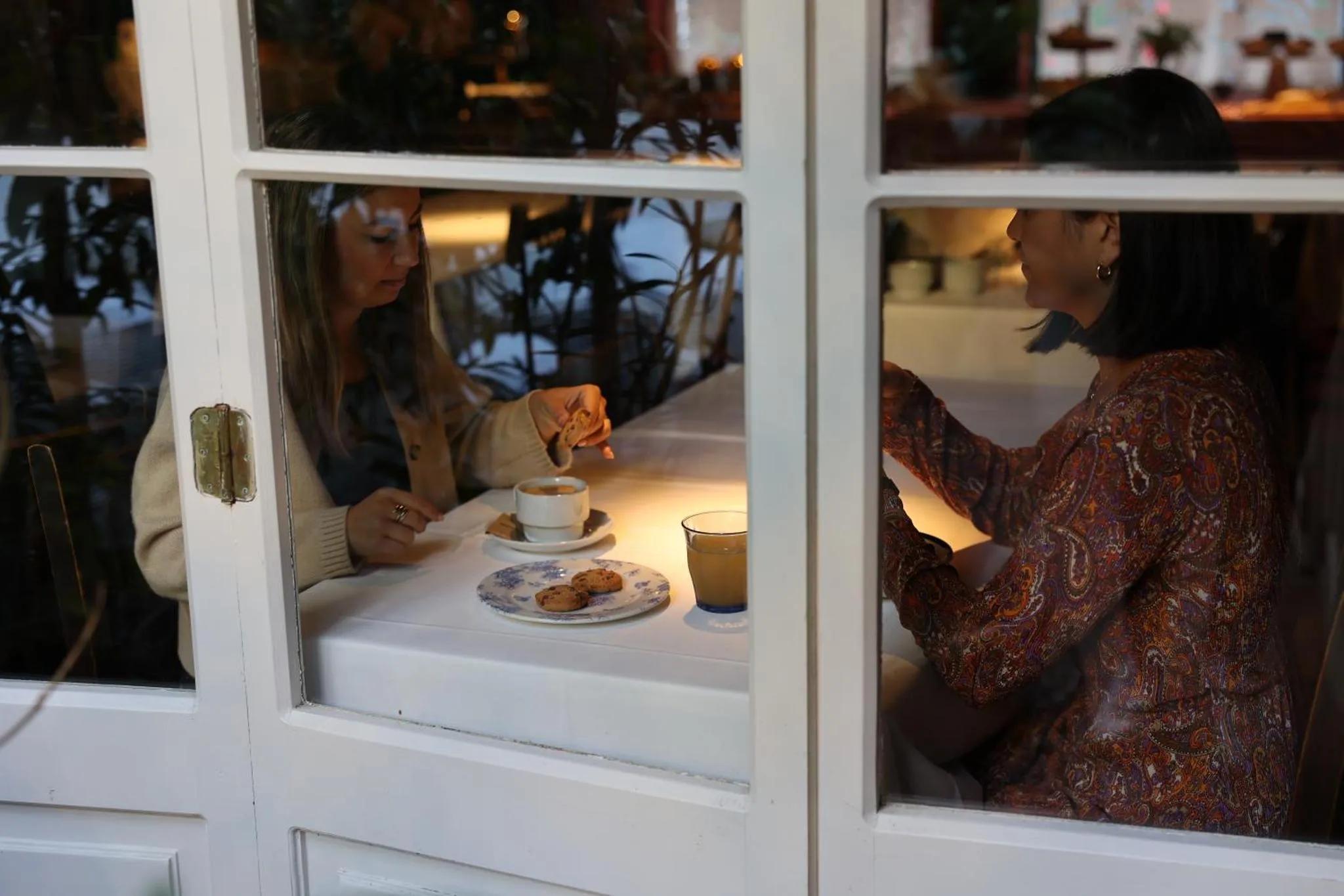 Deux femmes sont assises à une table et dégustent des biscuits avec leurs boissons.