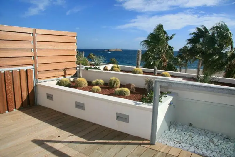 Terrasse en bois avec jardinières de cactus et vue sur la mer.
