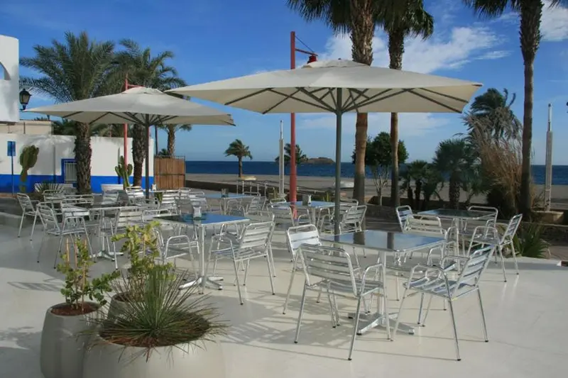 Terrasse ombragée avec tables et chaises en métal près de la mer.