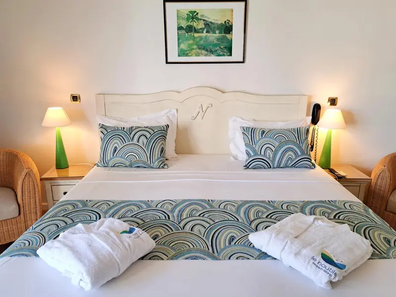 Lit double avec linge de lit bleu et vert dans une chambre lumineuse.