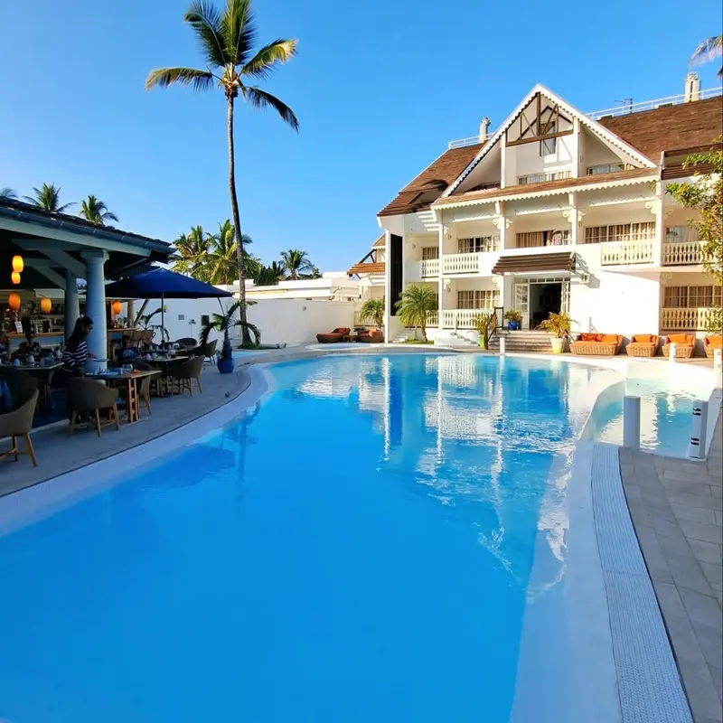 Une piscine turquoise reflète un bâtiment blanc à plusieurs étages sous un ciel bleu clair.