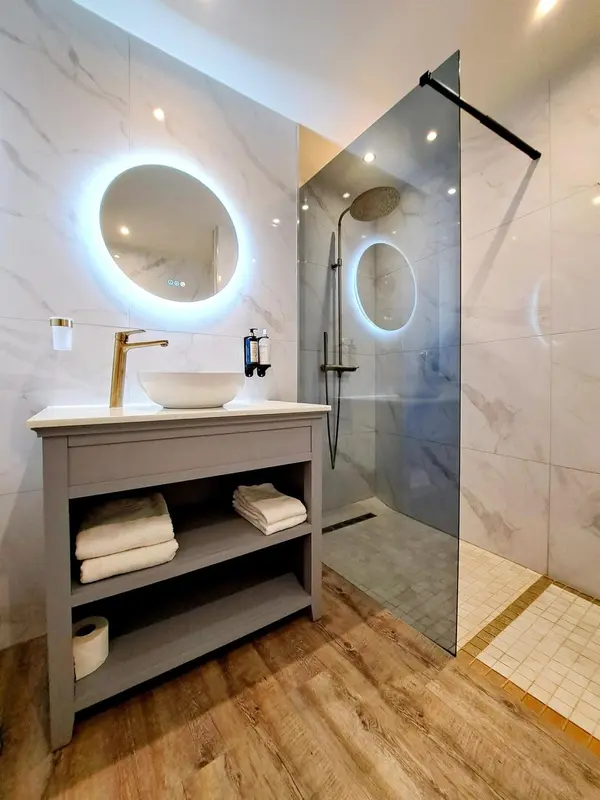 Une salle de bain moderne avec une douche à l'italienne et un miroir rond lumineux.