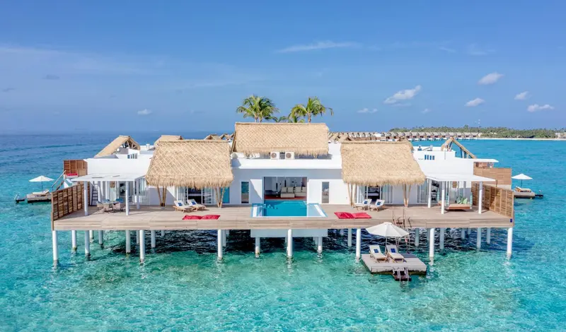 Vue aérienne d'une villa sur pilotis avec piscine et accès à la mer turquoise.