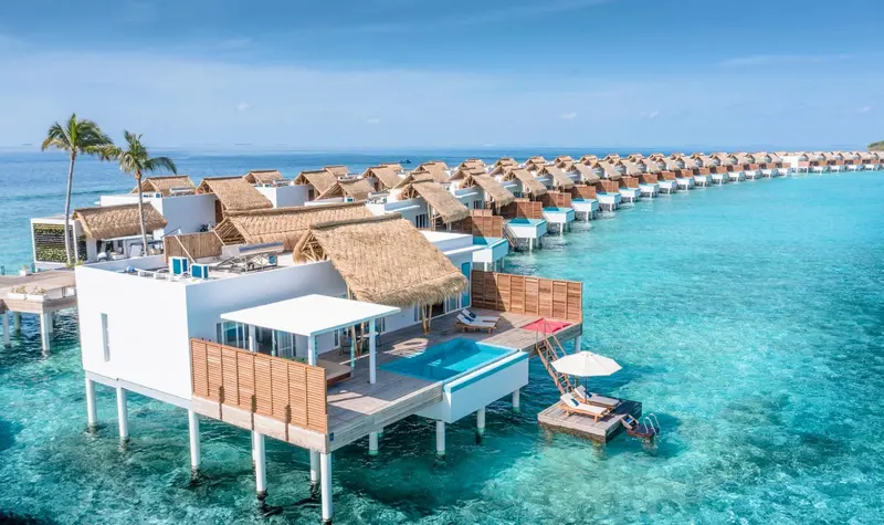 Vue aérienne d'une rangée de villas sur pilotis au-dessus d'une eau turquoise.