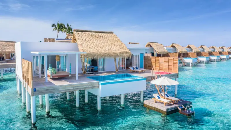 Maisons sur pilotis au-dessus d'une eau turquoise et d'une plage de sable blanc.