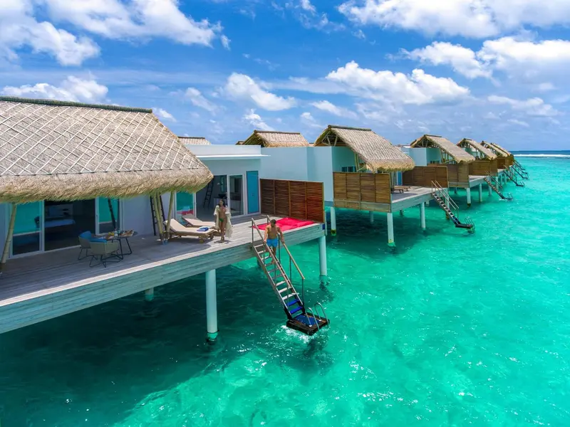 Plusieurs bungalows sur pilotis s'alignent sur une eau turquoise et claire.