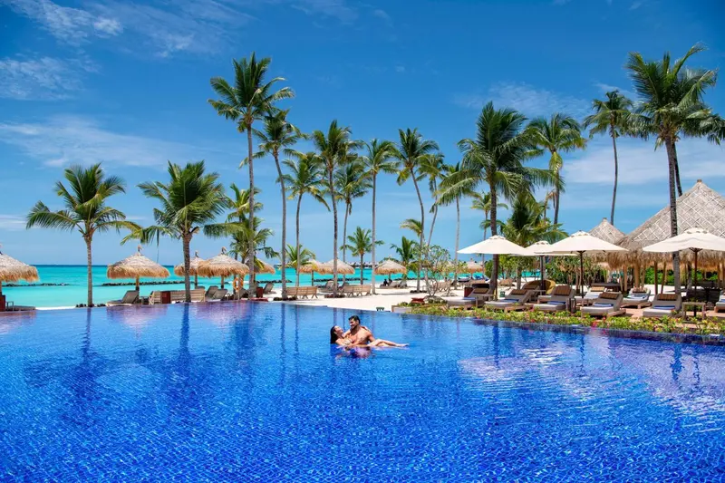 Une piscine bleue bordée de palmiers et de transats sous le soleil.