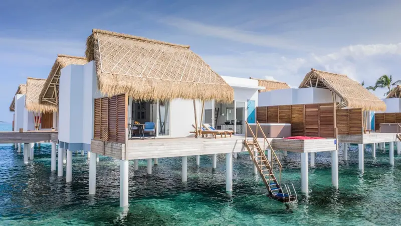 Plusieurs bungalows sur pilotis au-dessus d'une eau turquoise et claire.