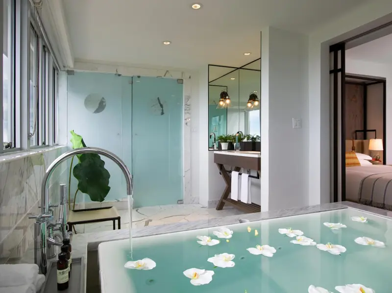 Une baignoire remplie d'eau et de fleurs blanches se trouve dans une salle de bain lumineuse.