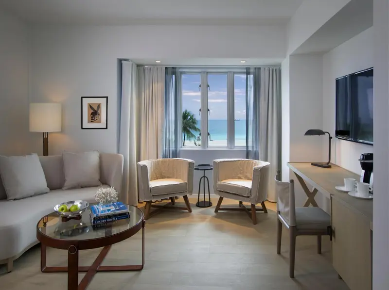 Espace de séjour lumineux avec canapés et fauteuils face à une grande fenêtre.