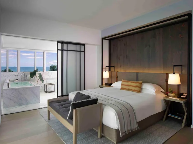 Une chambre lumineuse avec un grand lit et une baignoire à débordement donnant sur la mer.
