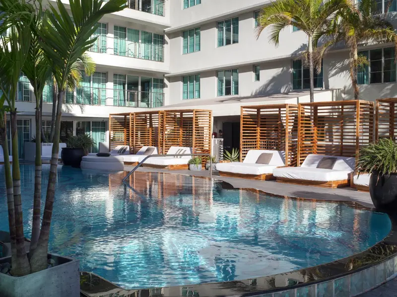 Une piscine bordée de cabanas en bois et de transats blancs.