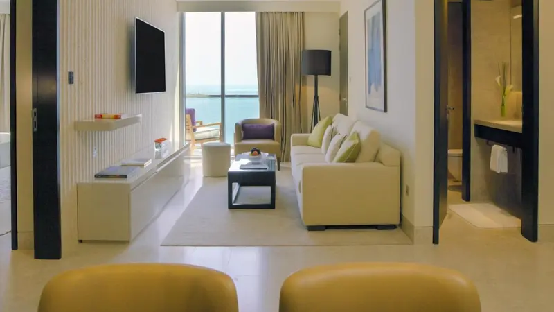 Un salon clair avec canapés et fauteuils face à une grande baie vitrée donnant sur la mer.