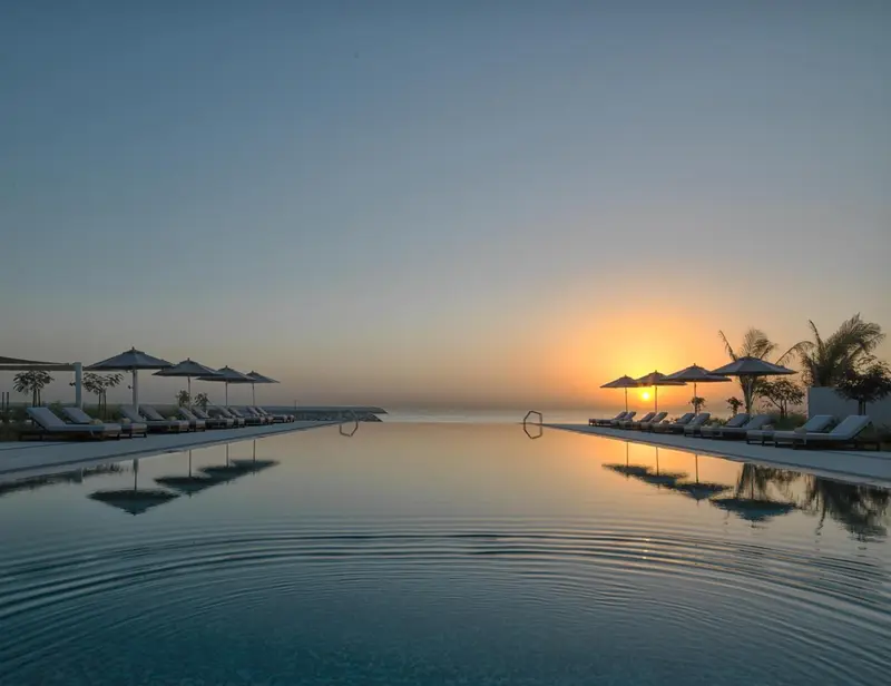 Une piscine à débordement reflète le ciel orangé du coucher de soleil.