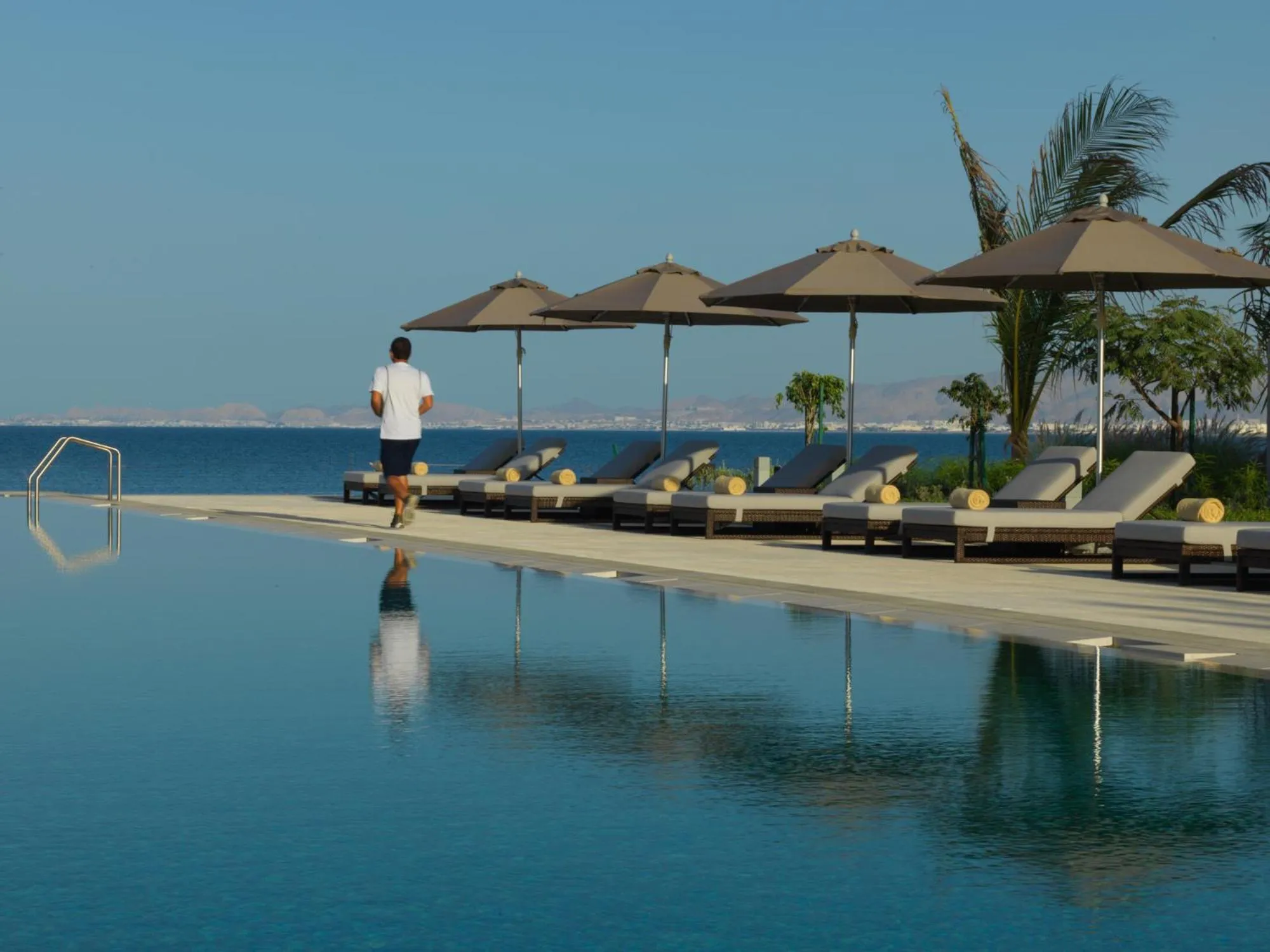 Une piscine à débordement offre une vue sur la mer et des transats ombragés.