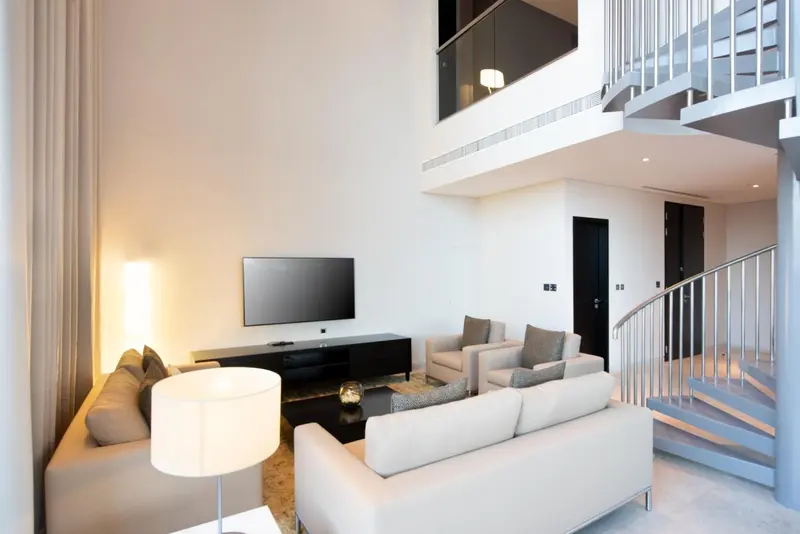 Un salon clair avec canapés, fauteuils et une télévision à écran plat.