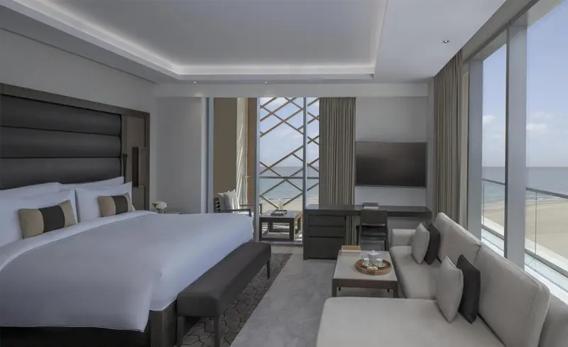 Chambre lumineuse avec un grand lit et un espace salon donnant sur la mer.