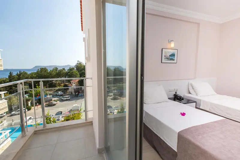 Chambre lumineuse avec un lit soigné et un balcon offrant une vue sur la mer et la végétation.