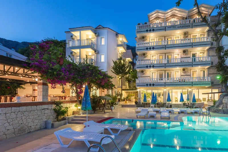 Bâtiment blanc à plusieurs étages illuminé la nuit avec une piscine au premier plan.