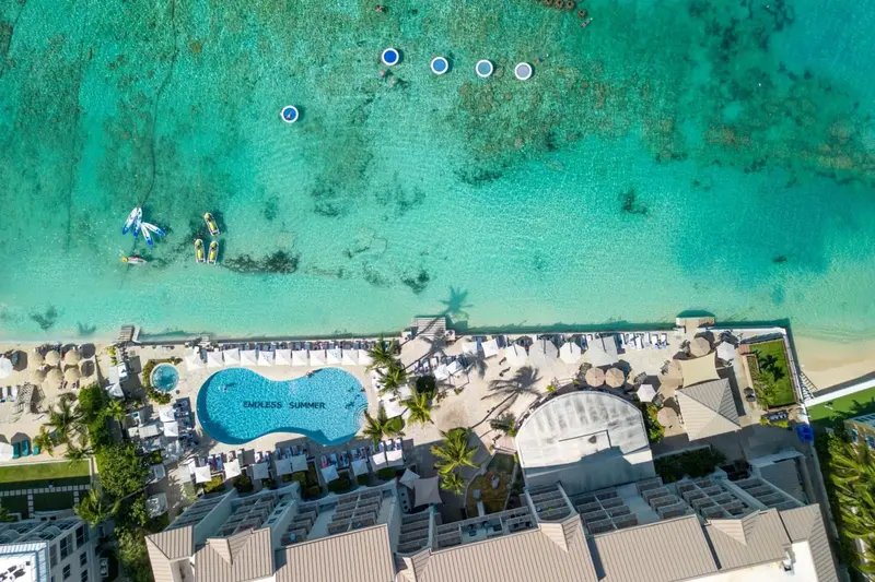 Vue aérienne d'un complexe hôtelier avec piscine et plage bordée de transats.