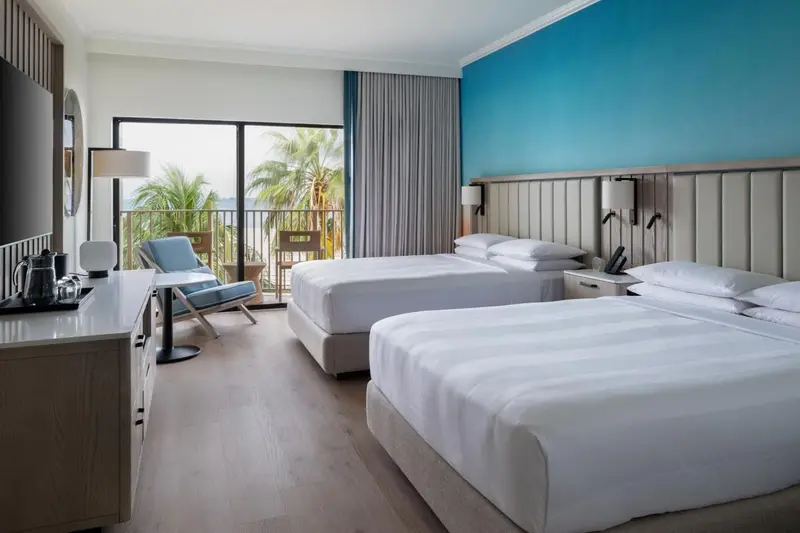 Une chambre lumineuse avec deux lits et une vue sur la végétation tropicale.