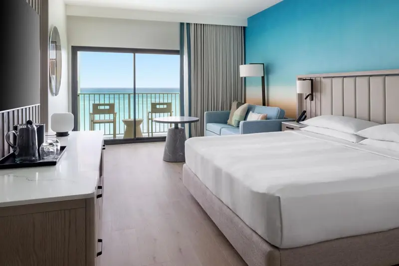 Une chambre lumineuse avec un grand lit et une vue sur la mer depuis un balcon.