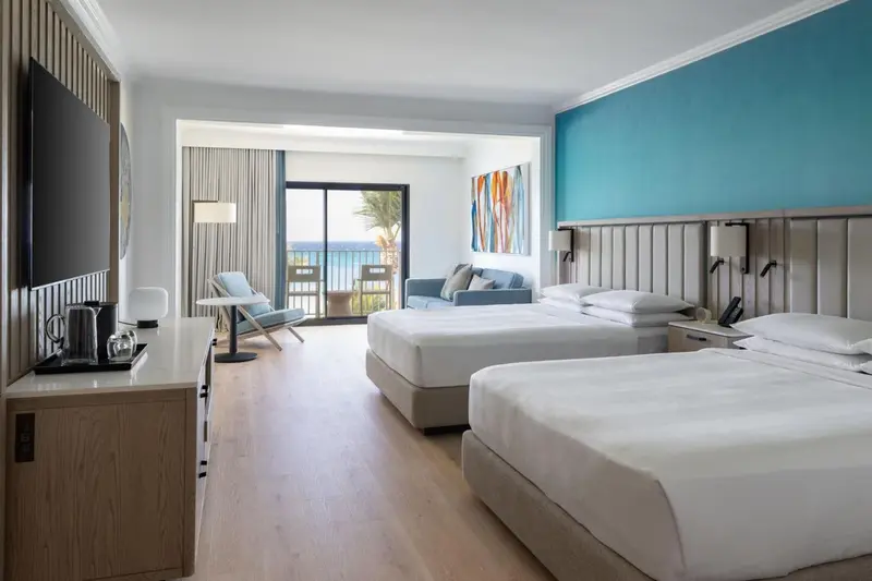 Chambre lumineuse avec lits jumeaux, canapé et vue sur la mer.