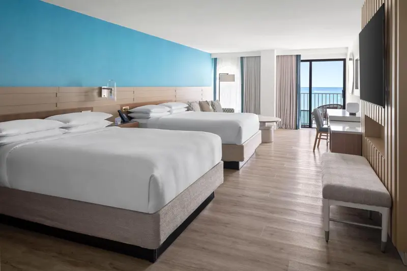 Chambre lumineuse avec deux lits et vue sur la mer.