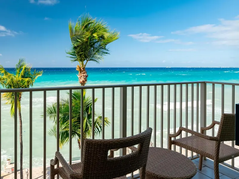 Terrasse avec mobilier en osier donnant sur une mer turquoise et des palmiers.