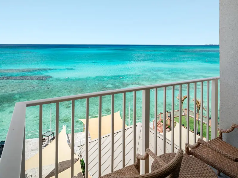 Vue sur une mer turquoise depuis un balcon avec des fauteuils.