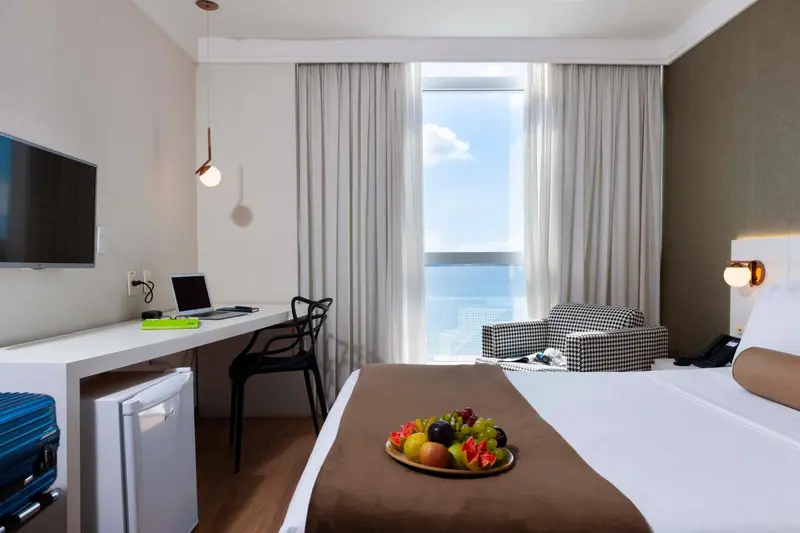 Une chambre lumineuse avec un bureau, un lit et une vue sur la mer.