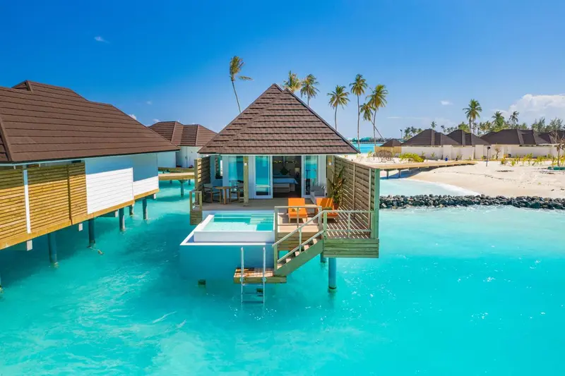 Maisons sur pilotis au-dessus d'une eau turquoise et d'une plage de sable blanc.