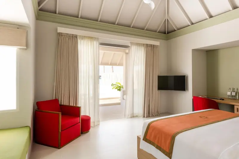 Une chambre lumineuse avec un fauteuil rouge et un lit recouvert d'une courtepointe.